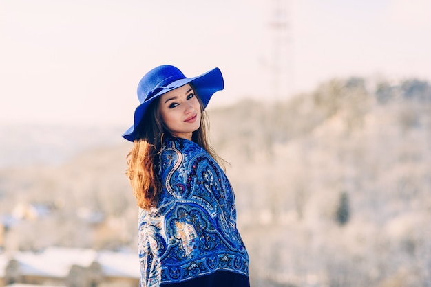 Belle jeune femme élégante en chapeau bleu et écharpe marchant dans le parc