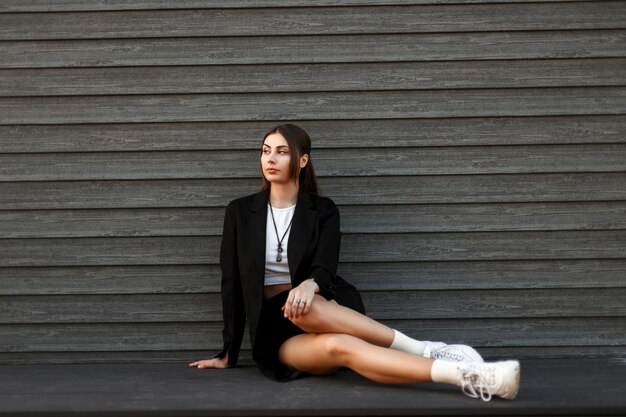 Belle jeune femme élégante dans un manteau noir avec des baskets à la mode blanches