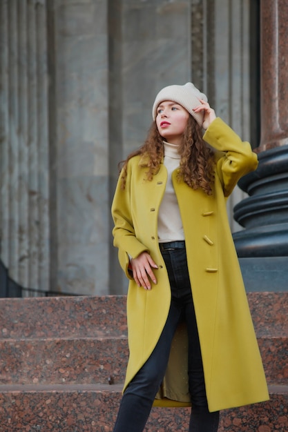 Belle jeune femme élégante à la mode en manteau jaune marchant dans la rue. Tendance de la mode d'automne pour une femme souriante, heureuse et déterminée. Objectifs de style conceptuel, de mode, de beauté et de réalisation. Espace de copie