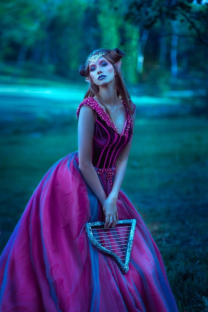 Belle jeune femme elfe vêtue d'une longue robe violette marchant dans la forêt d'été