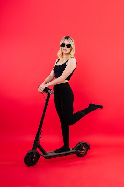 Belle jeune femme émotionnelle en vêtements de sport sur un scooter électrique sur fond rouge et blanc