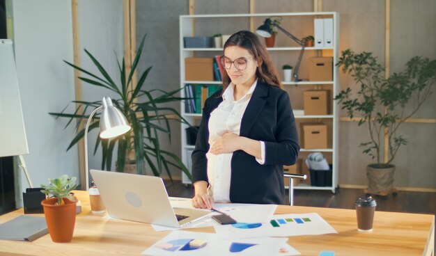 Belle jeune femme enceinte au travail dans un bureau moderne et confortable