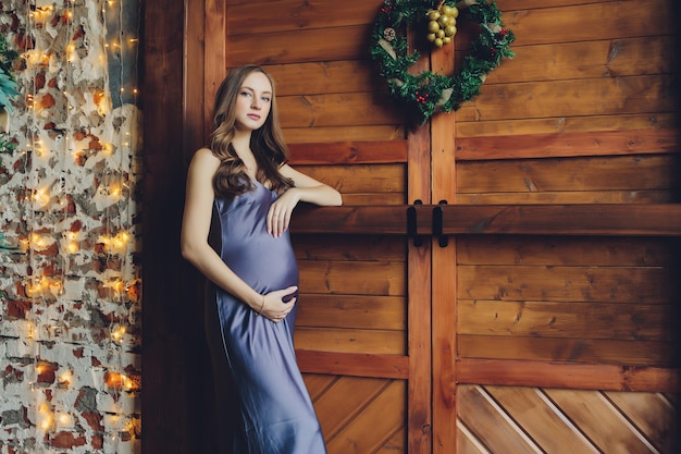 Belle jeune femme enceinte aux cheveux blonds et maquillage doux en robe rouge à la mode posant près du studio