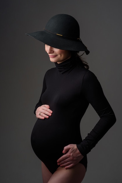 Belle jeune femme enceinte en body noir et chapeau.