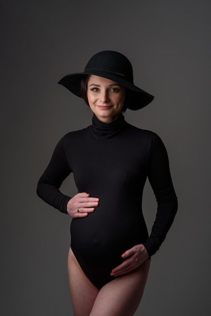 Belle jeune femme enceinte en body noir et chapeau.