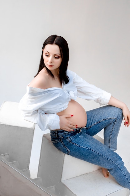 Photo belle jeune femme enceinte brune en blue-jeans étreint le ventre.