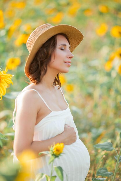Belle jeune femme enceinte dans le champ de tournesol. Portrait d'une jeune femme enceinte au soleil. Été.