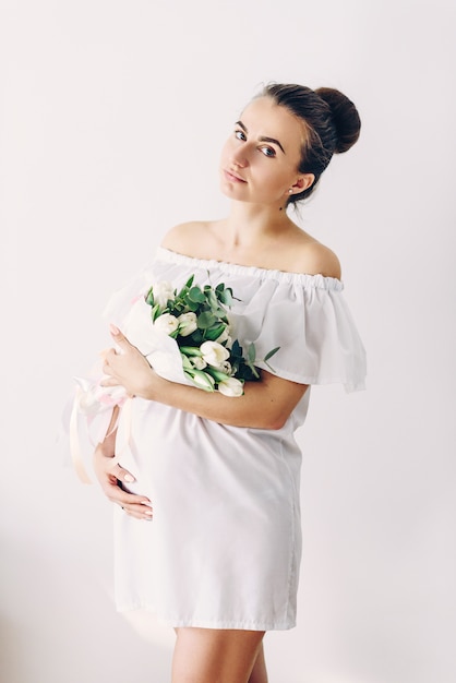 Belle jeune femme enceinte dans une robe blanche avec un bouquet de tulipes blanches