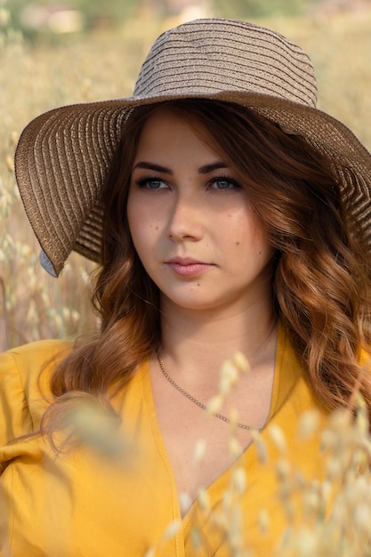 Une belle jeune femme enceinte dans une robe jaune et un chapeau se promène dans un champ de blé orange sur une journée d'été ensoleillée