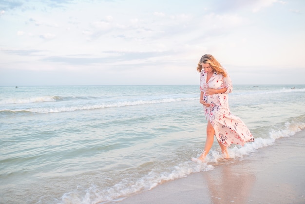 Belle jeune femme enceinte heureuse dans une robe légère d'été serrant son ventre