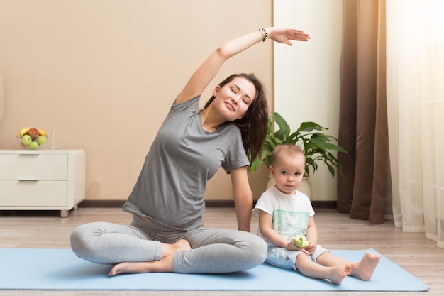 Belle jeune femme enceinte et petit garçon souriant en position couchée sur un tapis de yoga