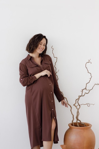 Une belle jeune femme enceinte vêtue d'une robe bordeaux sur fond blanc. Grossesse, un studio avec un fond vide.