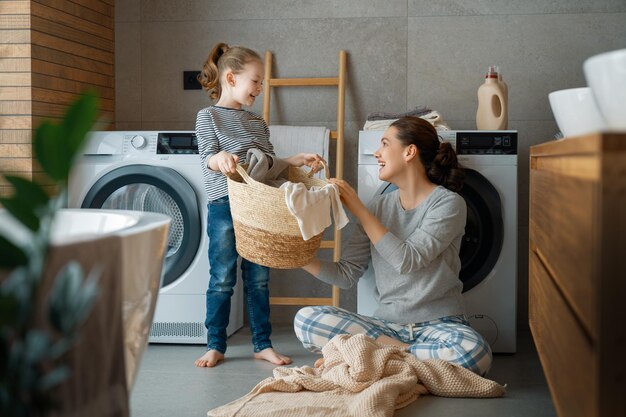 Belle jeune femme et enfant fille petite aide s'amusent et sourient en faisant la lessive à la maison