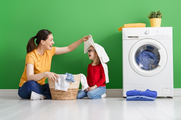 Photo belle jeune femme et enfant fille petite aide sourient en faisant la lessive à la maison
