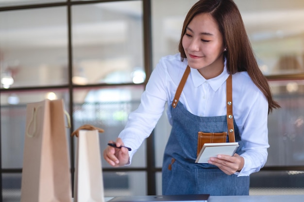 Une belle jeune femme entrepreneur avec tablier vérifiant les commandes du client