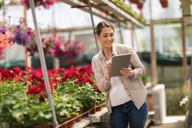 Belle jeune femme entrepreneur travaillant dans une jardinerie ou une pépinière et écrivant sur un presse-papiers de tablette.