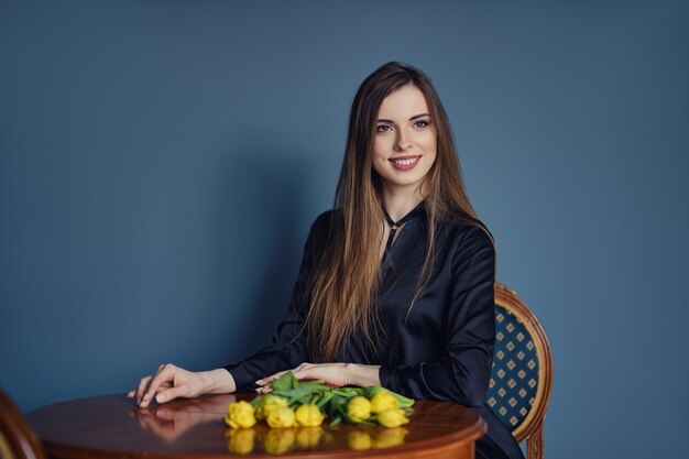 Belle jeune femme est assise derrière la table avec des tulipes