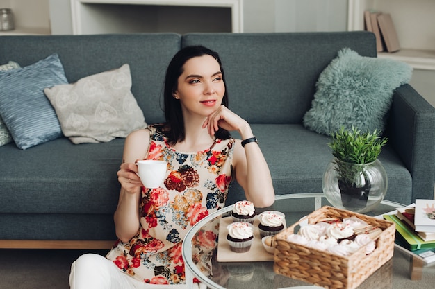 Belle jeune femme est assise sur un sol et pense à quelque chose et boit un salon de thé chaud et pense à son avenir avec une tasse de café