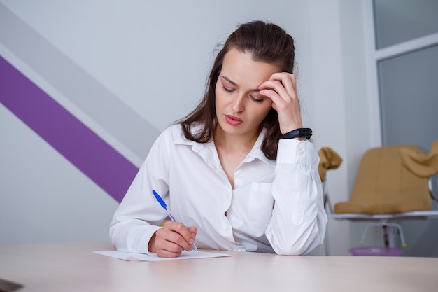 Une belle jeune femme est assise à une table et signe des documents importants.