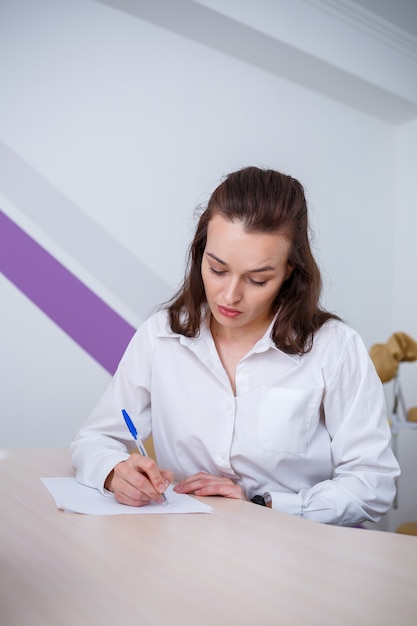 Une belle jeune femme est assise à une table et signe des documents importants.