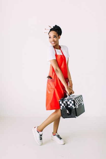 Belle jeune femme esthéticienne afro-américaine tenant ensemble d'équipement de maquillage dans un cas spécial, isolé sur fond blanc