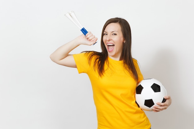 Belle jeune femme européenne joyeuse, fan de football ou joueur en uniforme jaune tenant un tuyau de football, ballon isolé sur fond blanc. Sport, jouer au football, santé, concept de mode de vie sain.