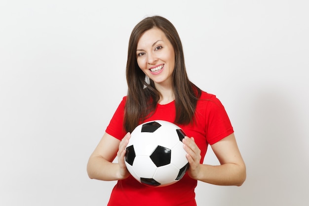 Belle jeune femme européenne joyeuse, fan de football ou joueur en uniforme rouge tenant un ballon de football classique isolé sur fond blanc. Sport, jouer au football, santé, concept de mode de vie sain.