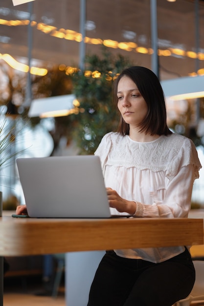 La belle et jeune femme européenne travaille sur son ordinateur portable dans un café ou un lieu public