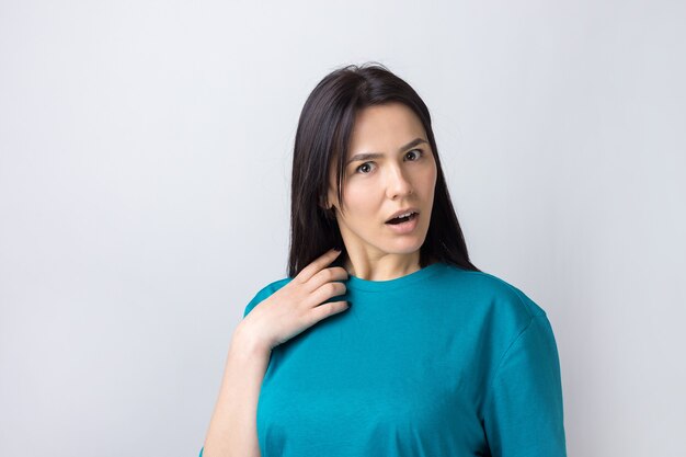 Belle jeune femme avec une expression faciale de surprise debout sur fond gris.