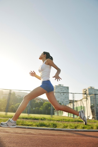 belle jeune femme faisant du jogging et de la course à pied sur une piste d'athlétisme sur le stade au lever du soleil