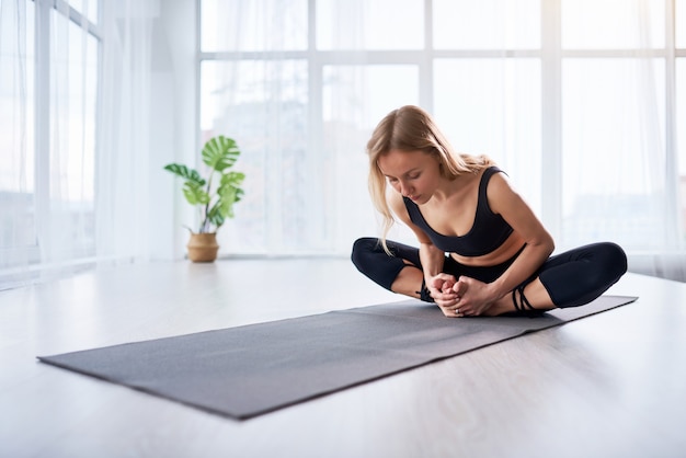 Belle jeune femme faisant du yoga dans une pièce lumineuse moderne avec de grandes fenêtres. Yoga à la maison.