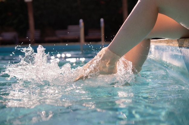 Belle jeune femme faisant des éclaboussures d'eau avec ses pieds au bord de la piscine Profitant de l'ambiance des vacances d'été Pas d'espace de copie de visage