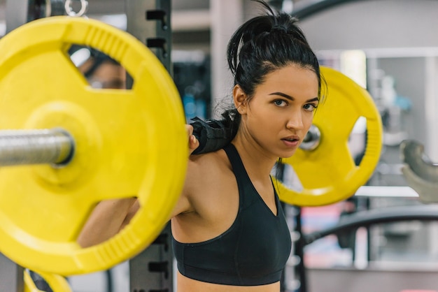 Photo belle jeune femme faisant de l'exercice dans la salle de gym en poussant des haltères jaunes sur les épaules