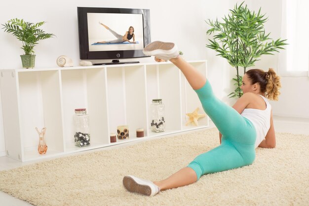 Belle jeune femme faisant de l'exercice à la maison en suivant les instructions à la télévision