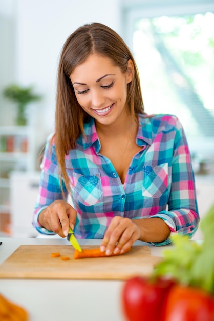 Belle jeune femme faisant un repas sain dans la cuisine domestique. Elle coupe la carotte sur le plateau de la cuisine.