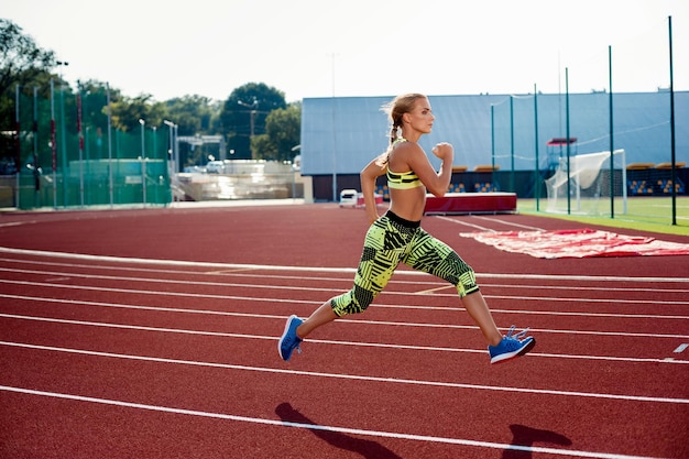 Belle jeune femme fait du jogging et de la course sur piste d'athlétisme sur le stade