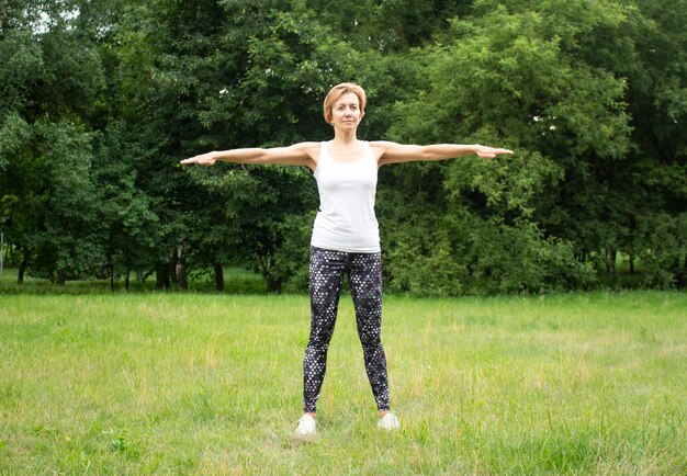 Belle jeune femme fait du sport dans le parc dans la nature. La femme est engagée dans le fitness en vêtements de sport. Mise en charge. Élongation.