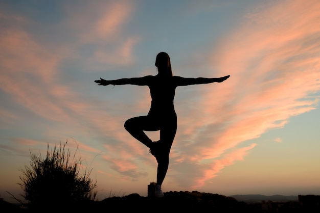 Belle jeune femme fait du yoga à l'extérieur, au sommet d'une crête de montagne dans la ville.