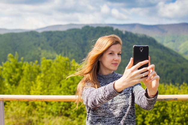 Photo la belle jeune femme fait le selfie à son téléphone sur le fond de la nature verte