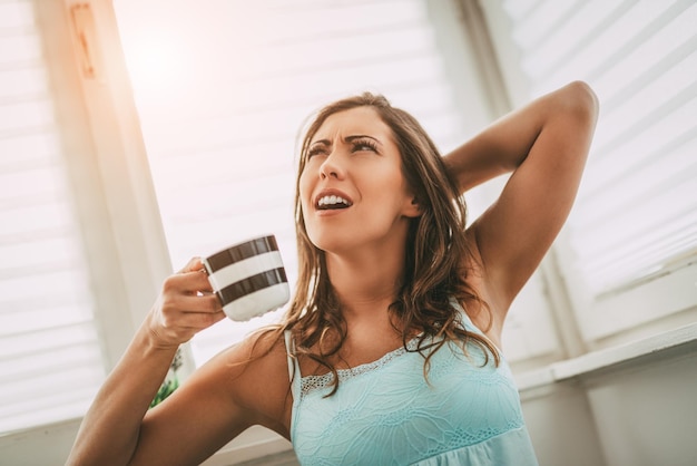 Belle jeune femme fatiguée qui boit du café le matin et ne peut pas se réveiller.