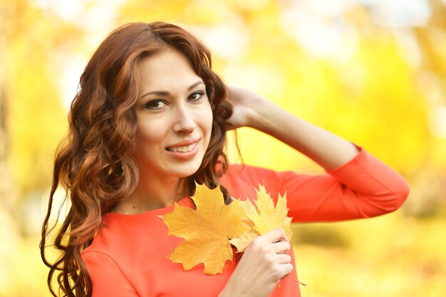 Belle jeune femme avec des feuilles posant dans le parc d'automne