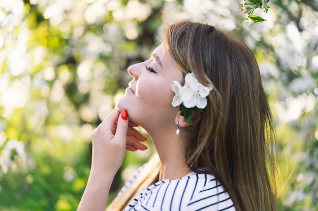 Belle jeune femme avec des fleurs de printemps profitant de la nature et riant sur le jardin de printemps