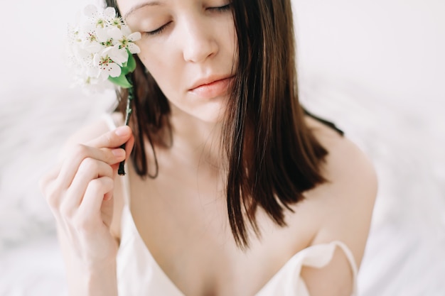 Belle jeune femme avec des fleurs sur une surface blanche