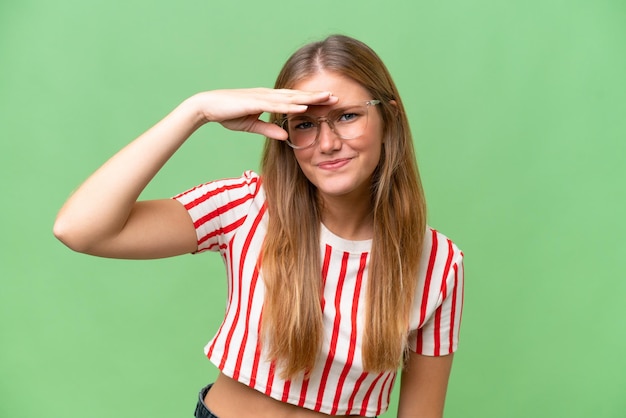 Belle jeune femme sur fond isolé à la recherche de loin avec la main pour regarder quelque chose