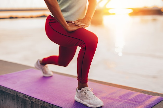 Belle jeune femme en forme et en bonne forme s'exerce seule dans la rue du pont de la ville. Elle écoute de la musique avec des écouteurs. Beau coucher de soleil en arrière-plan.