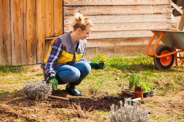 Belle jeune femme en gants travaillant sur le sol près de sa maison Premiers travaux de jardin de printemps