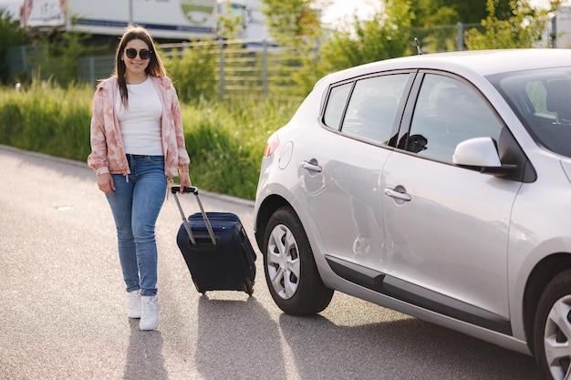 Belle jeune femme a garé la voiture et se rend à l'aéroport avec une valise