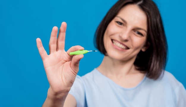 Belle jeune femme heureuse à l'aide d'une brosse interdentaire sur fond bleu