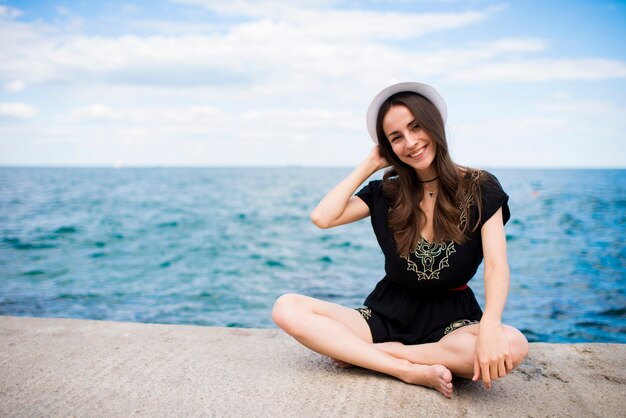 Belle jeune femme heureuse dans un chapeau repose sur le bord de la mer