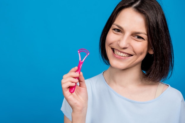 Belle jeune femme heureuse avec un gratte-langue sur fond bleu blanc